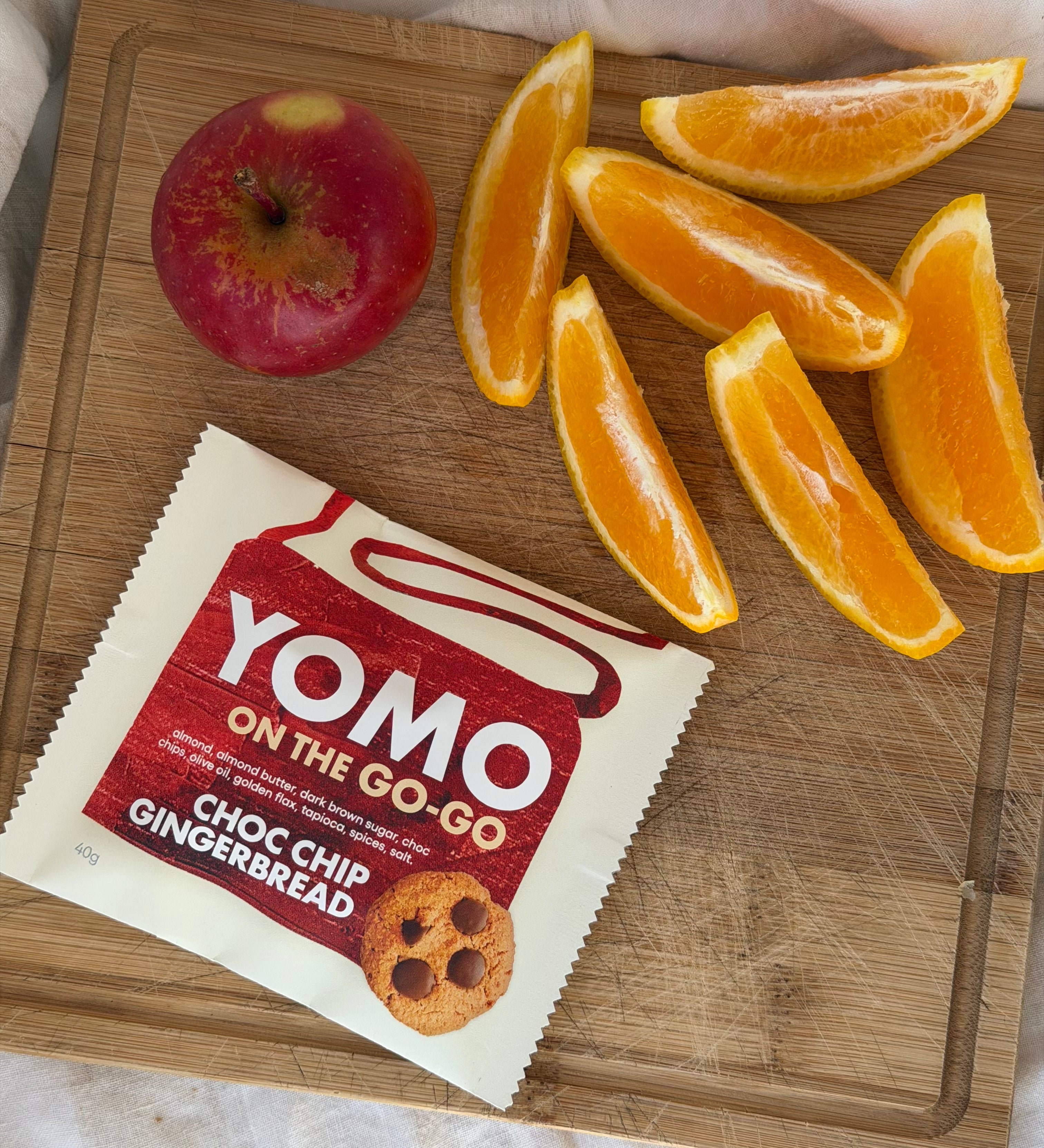 YOMO gluten free cookie on the go-go gingerbread, pictured for afternoon tea with orange slices and an apple on a wooden cutting board.