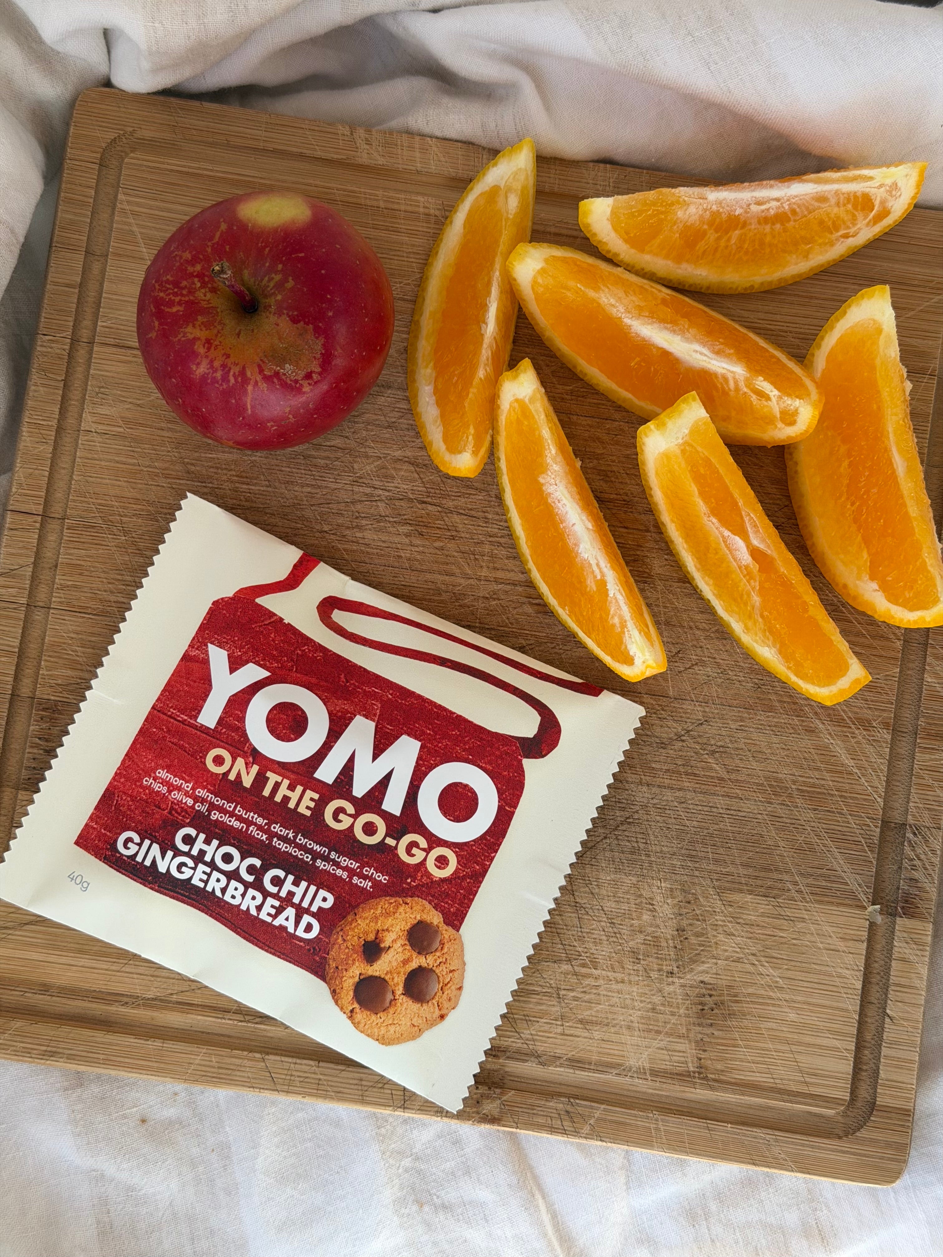 YOMO gluten free cookie on the go-go gingerbread, pictured for afternoon tea with orange slices and an apple on a wooden cutting board.